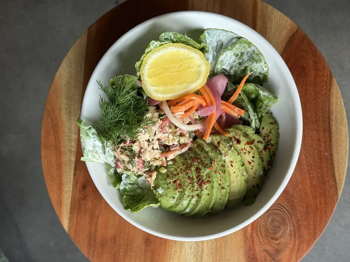 Little gem salad in a white bowl with sliced avocado, pickled onion, carrot, dill, and a lemon half