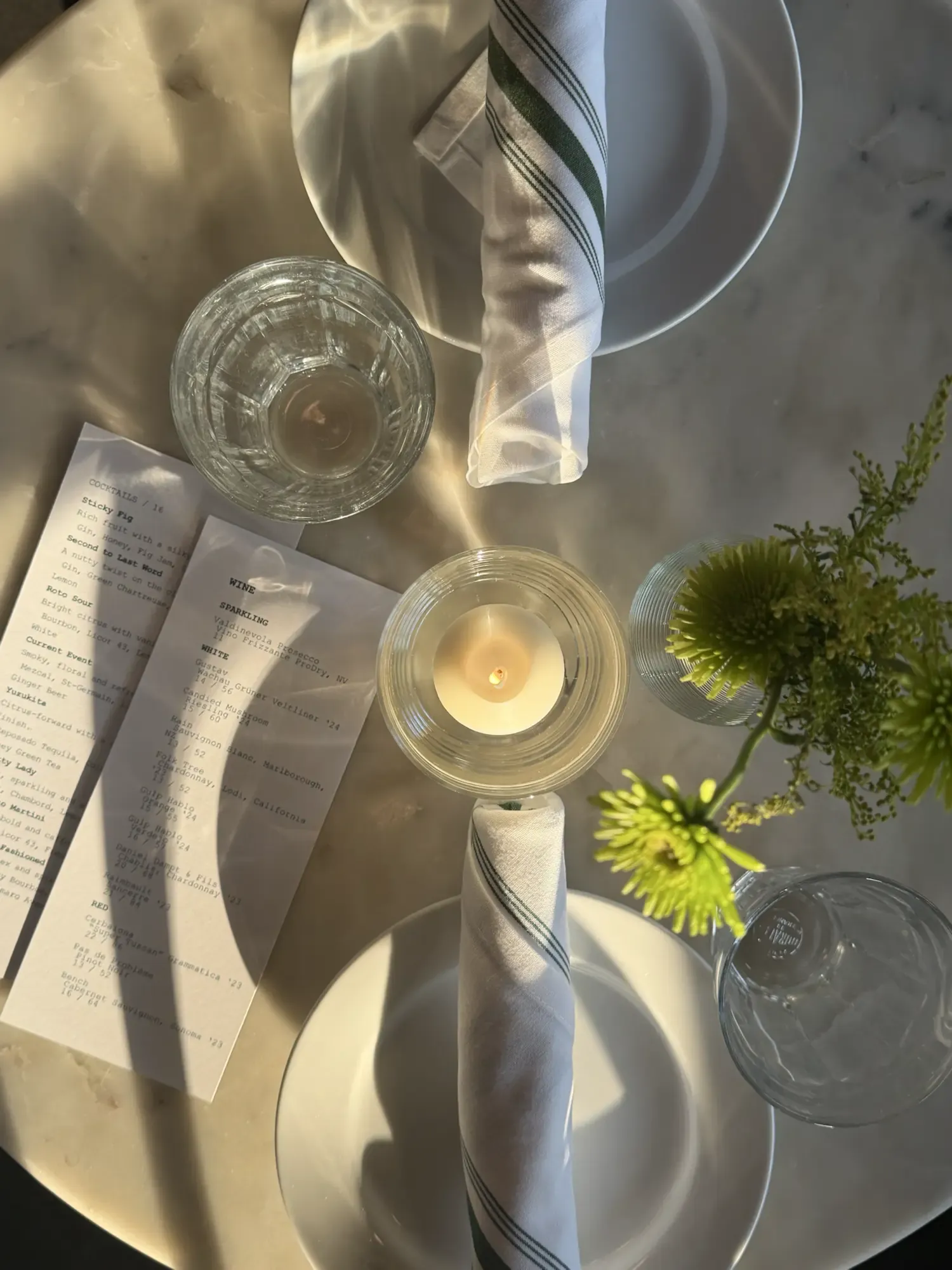 An overhead view of a Roto All Day table set with menus, glassware, and flowers